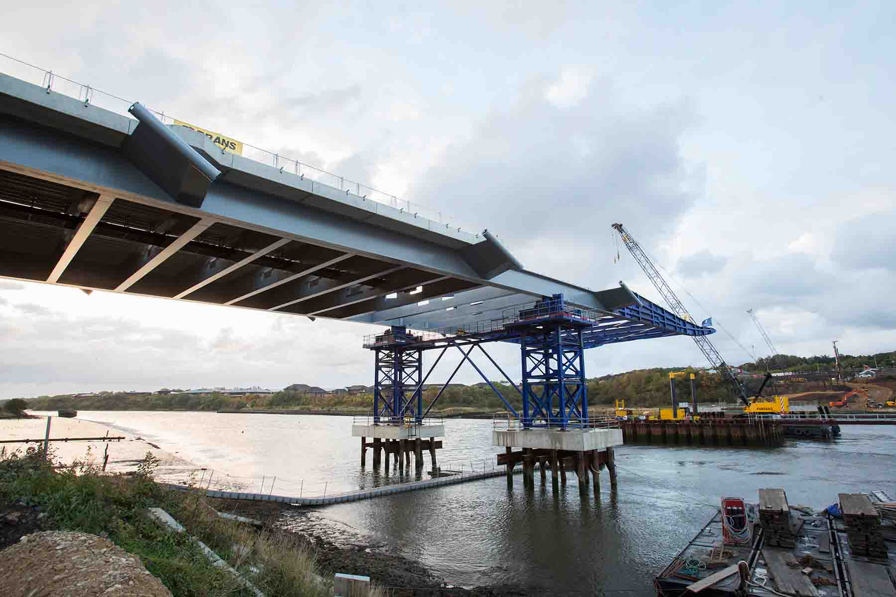 The first of two deck sections has been launched –slid – from the bank of the River Wear to rest balanced mid-river near the cofferdam into which the pylon’s foundations are being constructed
Sunderland’s New Wear Crossing project