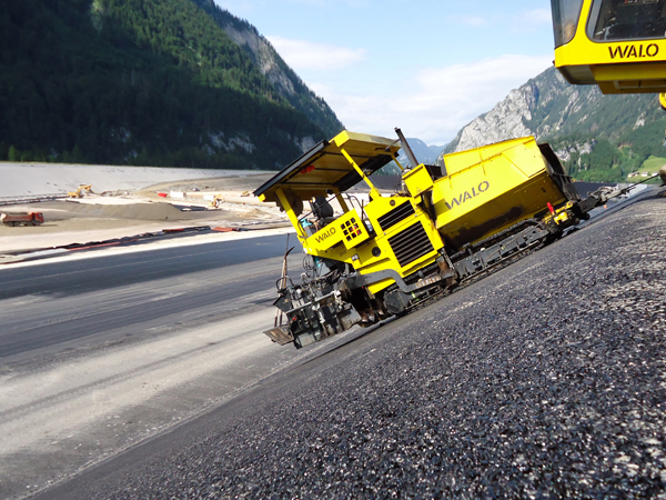 Two pavers are being winced down a slope to lay asphalt on the sides of a reservoir in Austria Volvo pavers working for WALO