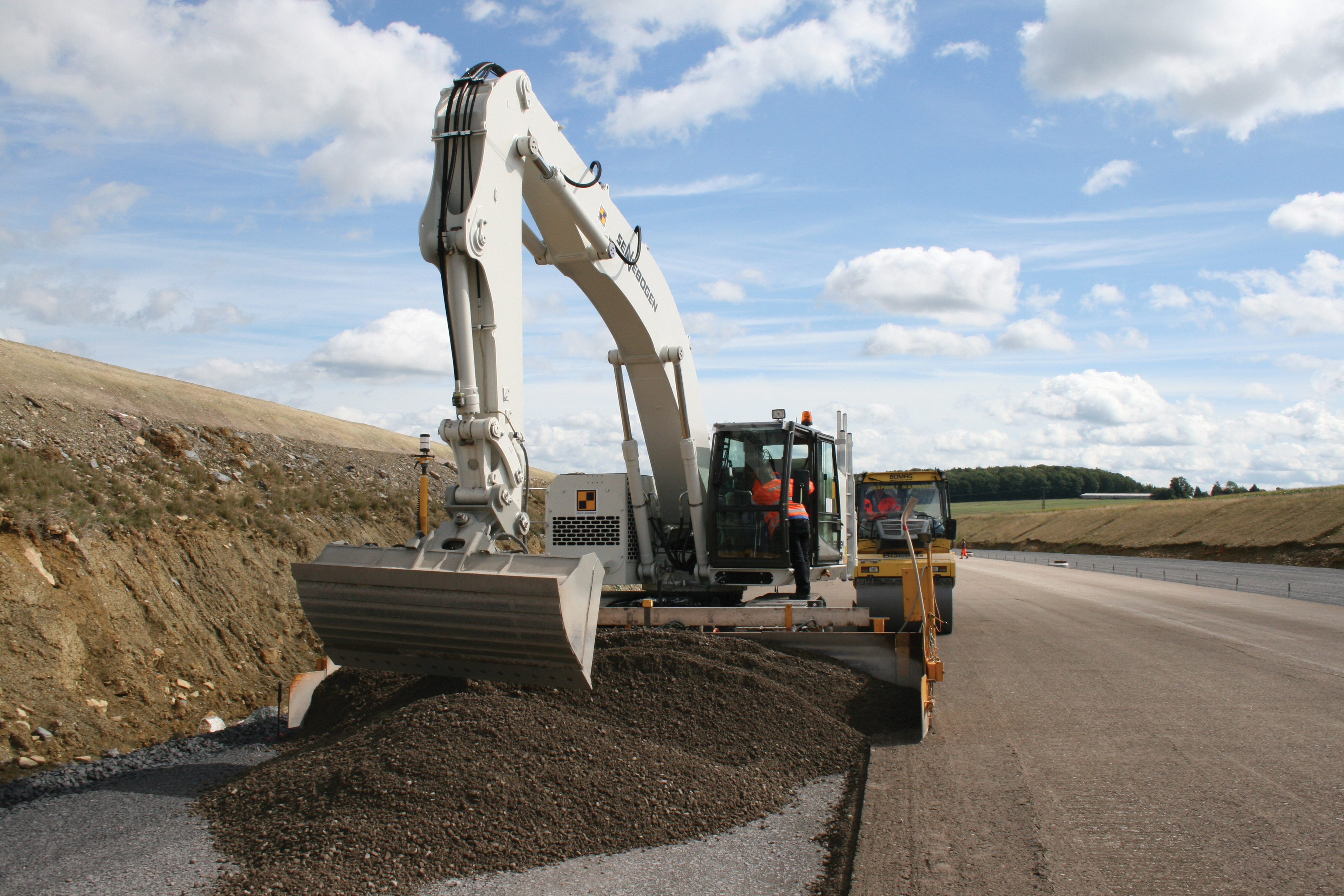 Automatic control mean the operator's prime function is to ensure material flow Excavator spreading concrete on road