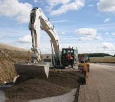 Excavator spreading concrete on road
